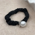 Detalle del coletero negro minimalista con tela texturizada y gran perla blanca central - Estilo de Perla Crema