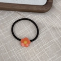 Nahaufnahme eines floralen Haargummis mit orangefarbenen Blüten auf Leinenhintergrund - Orange-Rosa Blumenhaargummi