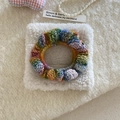 Close-up of handmade rainbow crochet hair tie with textured wool waves on cream fabric - Scrunchie Style / Colorful