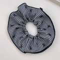 Detail eines großen Houndstooth-Scrunchie mit schwarzem Schleifenmuster und Stoffstruktur - Hahnentritt Haargummi