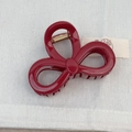 Macro detail of wine red bow-shaped hair claw clip with golden spring on textured fabric - Bowknot Style