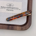 Detailed macro view of acetate hair clip featuring amber tortoise shell pattern and gold logo - Blue Brown Gradient