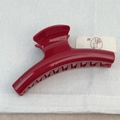 Close-up of a glossy deep red shark hair claw clip with fine glitter on white fabric - Hanger Style