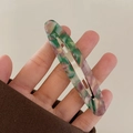 Dettaglio del fermaglio per capelli ovale in acetato marmorizzato tenuto in mano - Verde Pavone