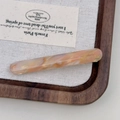 Macro detail of marbled acetate hair barrette with gold logo on woven texture display - Sakura Pink