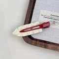 Macro detail of wavy cream resin hair clip with red metal base on a rustic fabric board - Off-white