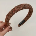 Detail of hand-made woven headband showing brown wool texture and orange metallic threads - Turmeric