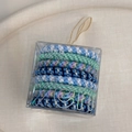 Close-up of multicolored braided elastic hair ties in a clear gift box with gold ribbon - Blue Series