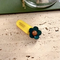 Makroansicht der handgefertigten Blumen-Haarklammer mit gelber Basis und grünem Dekor - Blaugrüne Blume
