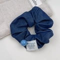 Nahaufnahme eines dunkelblauen Denim-Haargummis mit blauer Perle und gewebtem Etikett - Perlen Scrunchie