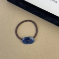 Detail of blue resin oval charm with gold lettering on a brown elastic hair tie - Blue