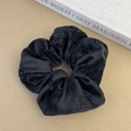 Detail view of black satin scrunchie with floral flocking texture on neutral background - Black