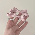Close-up of a pair of light pink satin bow hair clips held in hand for a delicate look - Pink