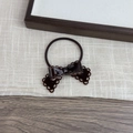 Detail of a dark brown hollow bow hair tie with glossy resin finish on soft linen fabric - Brown