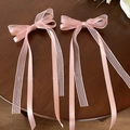 Close-up of pink satin and lace bow hair clips with long streamers on wooden surface - Pink