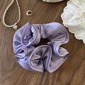 Elegant lavender purple satin scrunchie with soft pleats on a wooden background - Purple