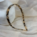 Dettaglio ravvicinato di un cerchietto sottile in acetato tartarugato su un vaso bianco - Leopardo Chiaro