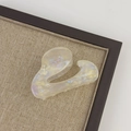 Detail view of small iridescent acetate shark hair claw with wavy design on linen background - Mermaid Color