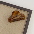 Close-up of small amber tortoiseshell hair claw with gold logo on beige fabric - Textured Brown