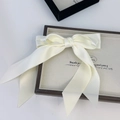 Macro shot of large cream satin double bow hairclip with long ribbons on a display tray - Off-white