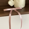 Gros plan détaillé d'une pince à cheveux à nœud en satin rose sur une étagère en bois - Rose