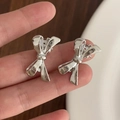 Par de pinzas para el cabello con lazo de metal plateado pulido sostenidas a mano - Lazo / Plateado