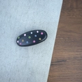 Detailed view of colorful polka dots on smooth black leather hair clip surface - Black Oval