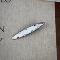 Détail d'une pince à cheveux crocodile en métal argenté avec des pois colorés sur tissu beige - Style Feuille