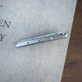 Vue détaillée d'une barrette argentée à pois colorés posée sur un tissu gris - Argent Fin Droit