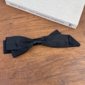 Detailed view of a large black satin bow hair clip on a wooden background with art books - Black