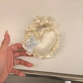 Dettaglio di un elastico in raso crema con cuore a balze e fiocchi di seta celeste - Cuore Bianco
