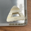 Macro détaillée d'une pince à cheveux triangulaire marbrée crème avec logo doré - Beige