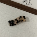 Détail d'une pince à cheveux ondulée en acétate avec motif écaille noir et blanc et logo doré - Écaille Claire