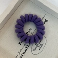 Macro shot of a purple knitted spiral hair tie showing soft braided texture and elastic design - Purple