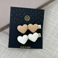 Vue détaillée de deux pinces à cheveux coeur mat en kaki et crème sur carte de support - Cœurs Café Au Lait (Paire)