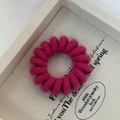 Close-up of a rose pink knit-wrapped spiral telephone wire hair tie in a wooden tray - Rose Red