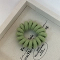 Close-up of a green knitted spiral hair tie on a white wooden display tray - Milky Green