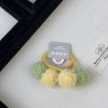 Gros plan d'élastiques à cheveux pompon pastel sur un fond de tissu texturé pour filles - Élastique Cheveux Balle Verte Et Jaune