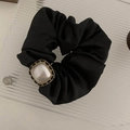 Gros plan d'un chouchou en satin noir avec perle vintage et détail de chaîne dorée - Noir