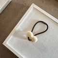 Dettaglio di un ciondolo a cuore in resina bianco crema su elastico marrone con sfondo strutturato - Beige