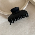 Detailed macro view of large matte black shark hair claw clip on beige fabric - Black Geometric