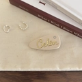 Details einer beigen matten Acetat-Haarspange mit goldener Schrift und Glitzerstein - Cremeweiß