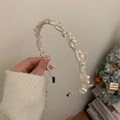 Dettaglio di un cerchietto crema elegante con perle e fiocchi delicati tenuto in mano - Bianco