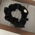 Minimalistisches schwarzes Satin-Scrunchie mit goldenem JW-Metallanhänger auf Holztablett - Schwarz