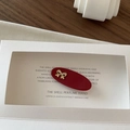 Detailed close-up of a red oval hair clip with a gold metal bow on a display card - Red