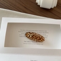 Detail view of a vintage leopard pattern hair clip with a gold metal bow on a display card - Leopard Print