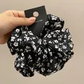 Dettaglio di un elastico per capelli in raso nero a fiori con trama a pieghe elegante - Nero