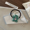 Détail de l'élastique ours vert et de la bague coeur argentée sur un tissu blanc doux - Cravate à cheveux / Vert Lac