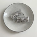 Nahaufnahme von silbernen Schleifen-Haarspangen auf Keramikteller, metallische Textur - Silber