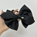Detalle de un gran lazo de satén negro para el pelo con una placa rectangular de metal dorado - Negro